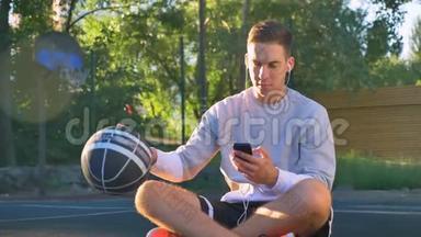 年轻人坐在<strong>篮球</strong>场上<strong>运球</strong>，通过耳机听音乐，拿着手机，露天